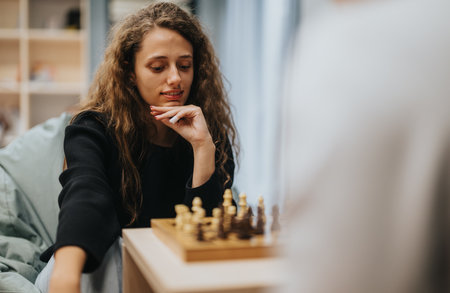 Young woman playing chess thoughtfully in a cozy room settingの写真素材