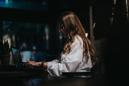 Focused businesswoman working on laptop at night in a dimly lit room