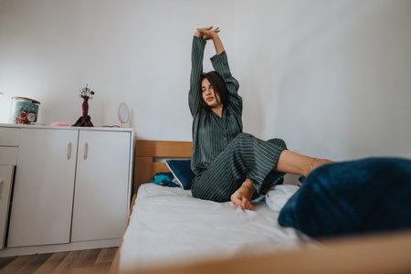 Woman stretching on bed in cozy pajamas during a relaxing morningの写真素材