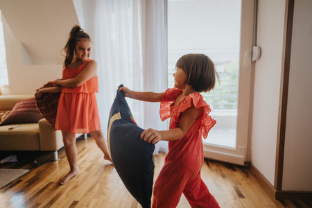 Joyful pillow fight between two sisters in a sunny living roomの写真素材
