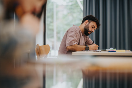 Male student intently writing in a classroom, highlighting focus and education.の写真素材