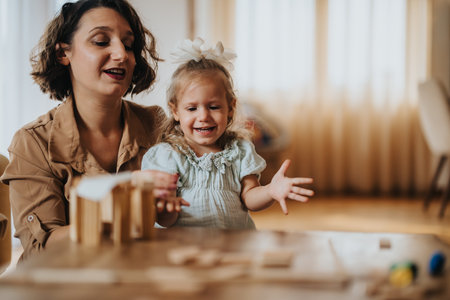 Mother and daughter laughing while playing with wooden blocks at homeの写真素材