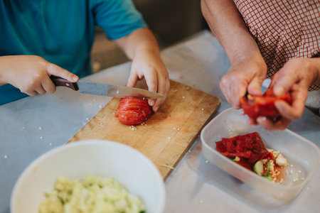 Child and adult cooking together in kitchen preparing fresh vegetablesの写真素材