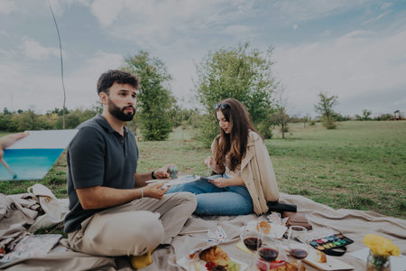 A couple paints together during a picnic in a scenic park, enjoying nature and creativity.の写真素材