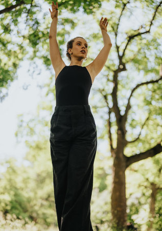 Beautiful young woman dancing in nature with arms raised, enjoying a sunny day outdoorsの写真素材