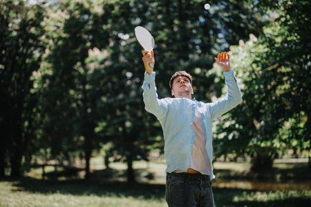 Young man playing paddle ball with friend in a sunny parkの写真素材