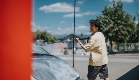 Young man washing car on a sunny day at car washの写真素材