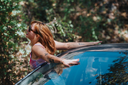 Joyful woman enjoying freedom with car sunroof in natureの写真素材