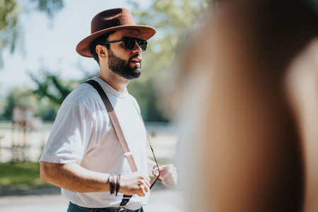 Man in casual attire with hat and suspenders enjoying a sunny day outdoorsの写真素材