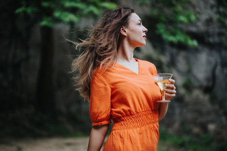 Young woman in orange dress enjoying picnic with champagne in natureの写真素材