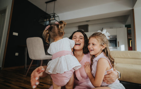 Happy mother playing with her daughters in the living room, sharing joyful momentsの写真素材