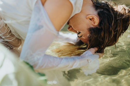 Woman leaning over water washing hair in serene natural settingの写真素材