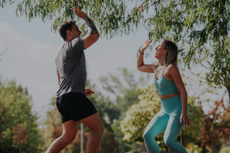 Two friends high-fiving during a sunny park workout sessionの写真素材