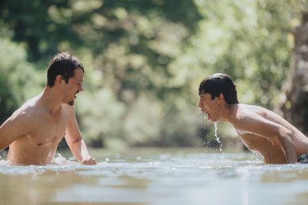 Two young men enjoying a fun swim in a natural settingの写真素材