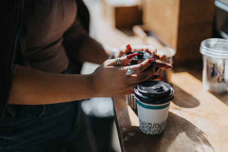 Person holding coffee cups with stylish rings in sunlight