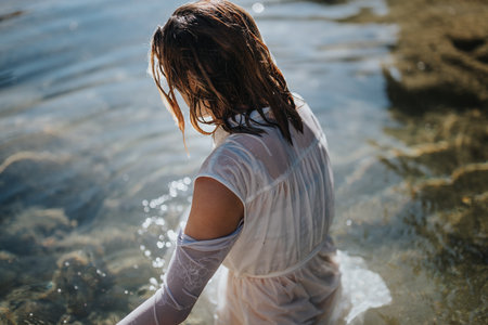Woman in white dress wading in clear water, enjoying a peaceful moment outdoorsの写真素材