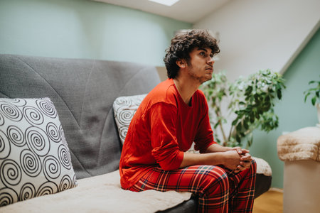 Young man in red sitting on a cozy modern sofa at homeの写真素材