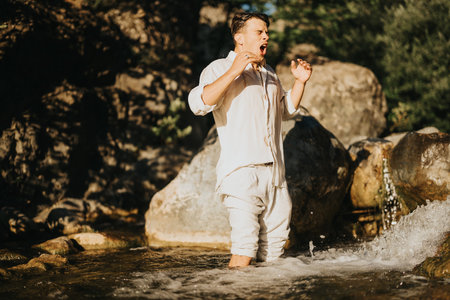 Man in white clothes standing in a river, expressing surprise in natural surroundings
