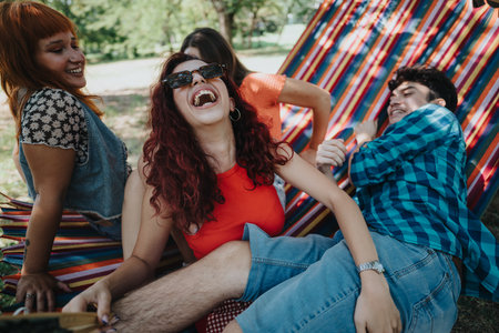 Group of friends laughing and enjoying a sunny day outdoors in a hammockの写真素材