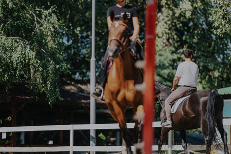 Men practicing horseback riding in a sunny outdoor equestrian arenaの写真素材
