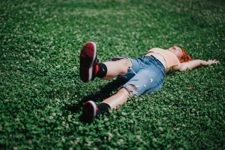 Young woman relaxing on sunny day in park on green grass, enjoying nature and freedomの写真素材
