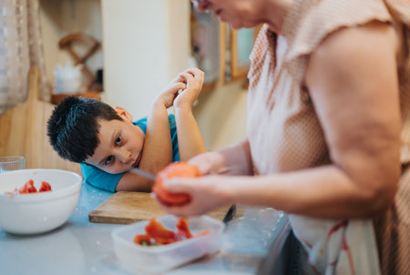 Child observing elder preparing food in home kitchen settingの写真素材