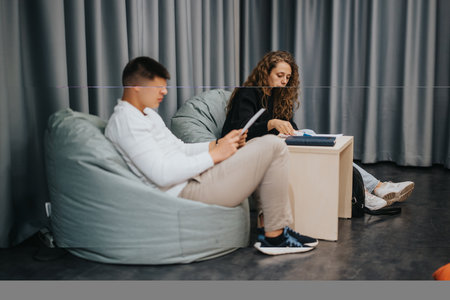 Two students studying in a relaxed setting, sitting on bean bags and reading books at school, fostering a calm and focused learning environment.の写真素材