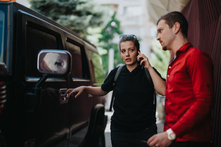 Two people standing beside a car, one talking on the phone while the other waits