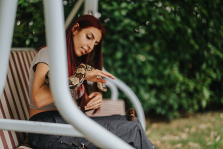 Girl with pet snake relaxing on an outdoor swing benchの写真素材