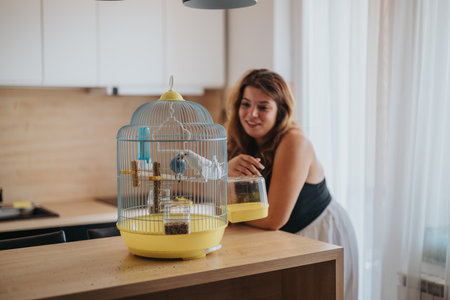 Woman smiling at a bird in a colorful cage at homeの写真素材