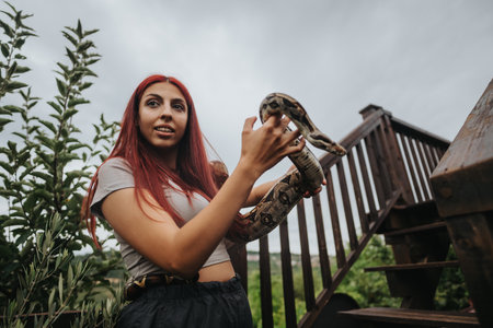 Girl holding a snake outdoor next to wooden stairsの写真素材