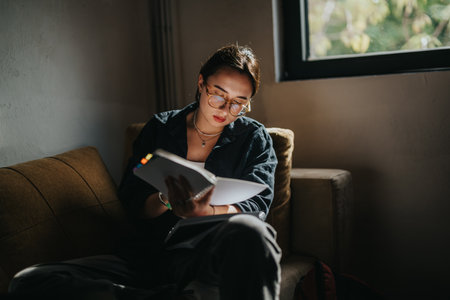 Young female student with glasses studying on a cozy sofa at home