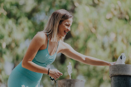 Smiling woman enjoying a refreshing outdoor fountain in the parkの写真素材