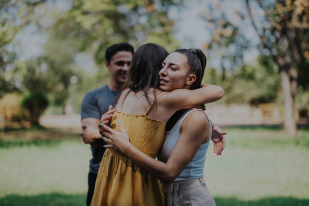 Two girls meet in the park, warmly welcoming each other with smiles and a friendly hug, excited to reconnect.の写真素材