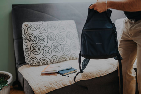 Man preparing backpack with notebooks on stylish sofa backgroundの写真素材