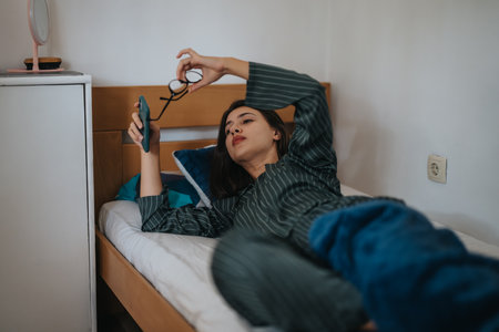 Woman relaxing on bed with smart phone in cozy bedroom settingの写真素材