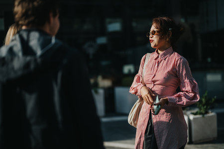Stylish woman in sunglasses having conversation outdoors in urban setting