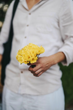 Person holding a bouquet of yellow flowers in a peaceful outdoor settingの写真素材