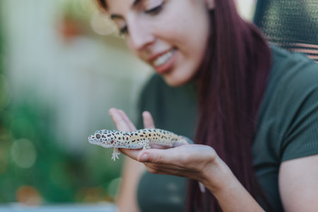 Young woman joyfully interacting with a leopard gecko in an outdoor garden setting, showcasing a bond with exotic pets and highlights the beauty of reptiles in natural surroundings under soft light.の写真素材