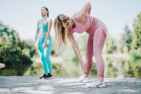 Two women exercising in a park, performing stretches and fitness routines on a sunny day, enjoying an active, healthy lifestyle surrounded by nature.の写真素材