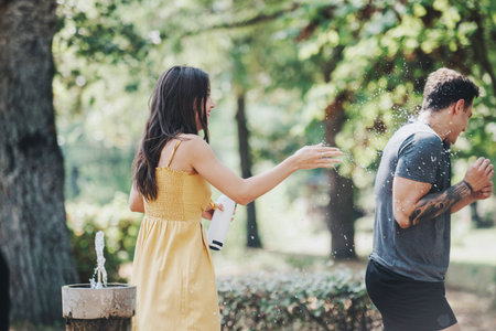Friends enjoying a playful water splash in a park during a summer day, embracing the fun moments of...