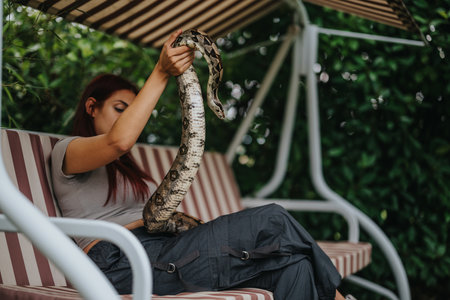 Girl with snake relaxing on swing under striped canopy