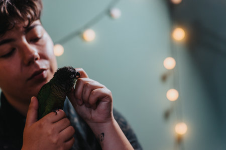 Young woman gently playing with a small parrot indoorsの写真素材