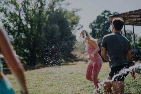Young friends enjoying a playful water fight outdoors on sunny day