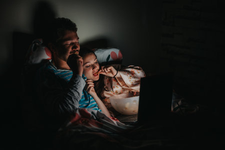Couple watching movie on laptop while eating in bed