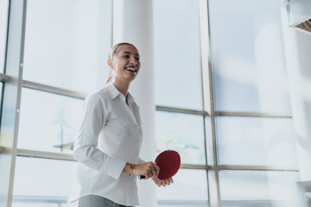 Confident businesswoman enjoying a fun table tennis break at officeの写真素材