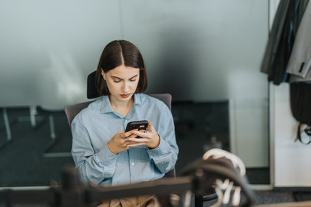 A young woman in a modern office setting is intently focused on her smart phoneの写真素材