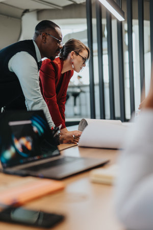 A diverse group of business colleagues engaging in a brainstorming session, discussing documents, and analyzing data for a collaborative project.の写真素材
