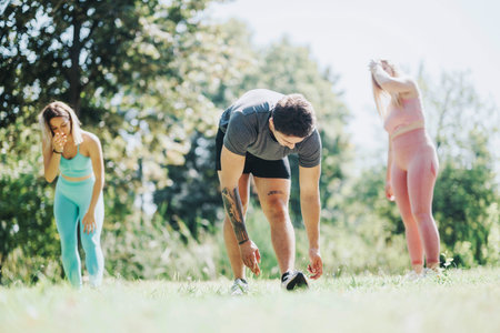 Group of young friends exercising together in a sunny park setting, stretching and warming up on a beautiful dayの写真素材