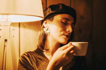 Pensive woman enjoying a quiet coffee moment under warm lightの写真素材